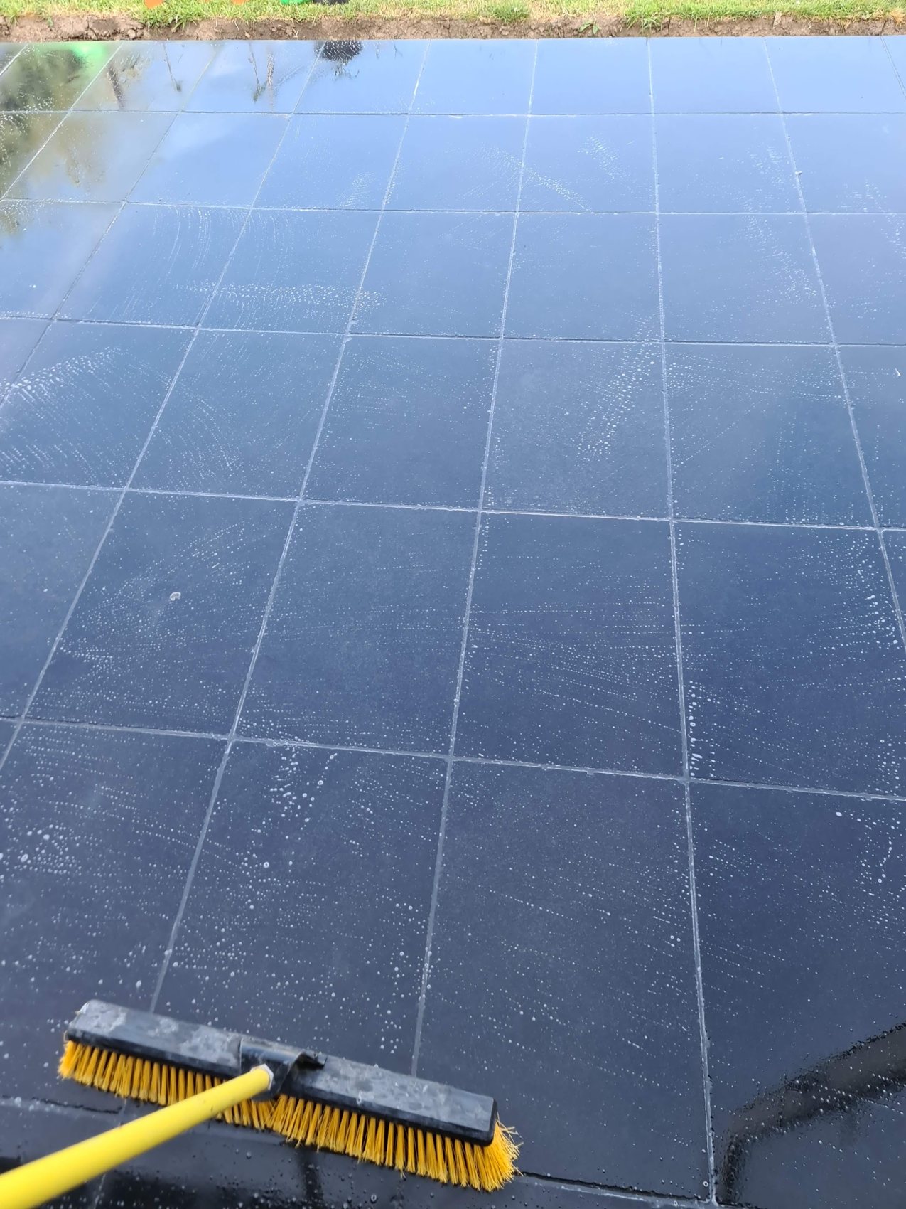 A dark slate paved surface being cleaned with a yellow brush